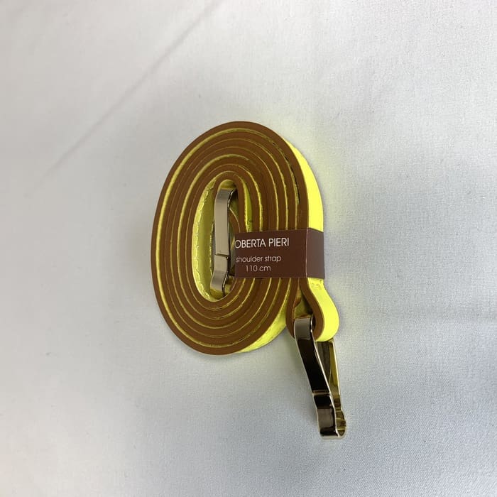 Der gelbe Schulterriemen mit goldenen Beschlägen ist gewickelt und auf der weißen Fläche ziert das braune "ROBERTA PIERI Schultergurt 110 cm"-Label.