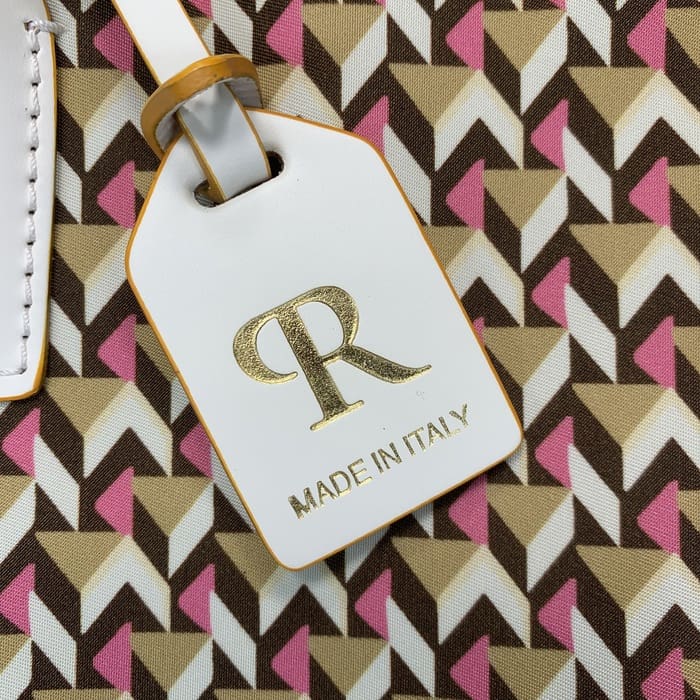 Nahaufnahme eines weißen Gepäckanhängers von Roberta Pieri mit dem Schriftzug "R" in Gold und den Worten "MADE IN ITALY", der an einem Mini-Seesack mit geometrischen Mustern in Braun, Beige und Rosa befestigt ist.