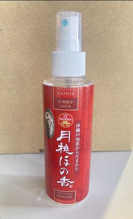 Eine rote Sprühflasche mit der Aufschrift "Nature Shower" auf beigem Hintergrund. Weiße Sprühdüse und Kappe.