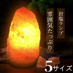 オレンジ色に輝く天然岩塩ランプ【サイズ：SS】— ほっと落ち着く、優しい間接照明が、暗い台座の上に置かれており、その横には日本語の文字と2つの岩塩が添えられている。ランプからは、温かみのある間接照明が放たれている。下部には白文字で「5サイズから選べます」と書かれている。.
